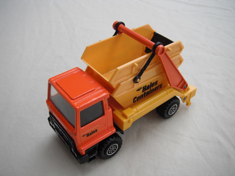 7.  Dark orange cab/type 1 cab roof/yellow skip/black base/hales label on cab door/large steering wheel.