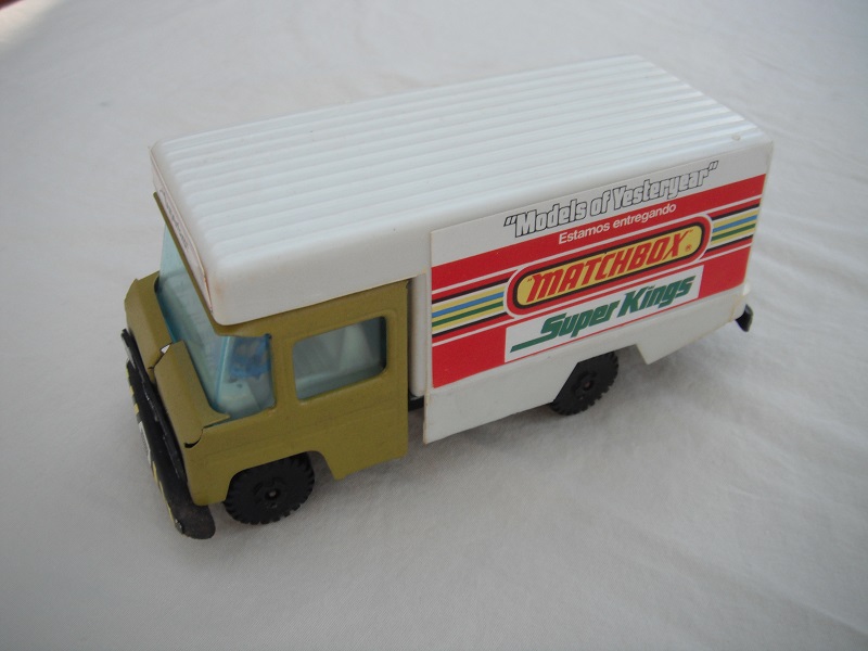 4. Olive green cab/white plastic body/metal base/black plastic wheels/clear windows/cream interior/blue steering wheel/labels w/various adverts of Matchbox ranges.