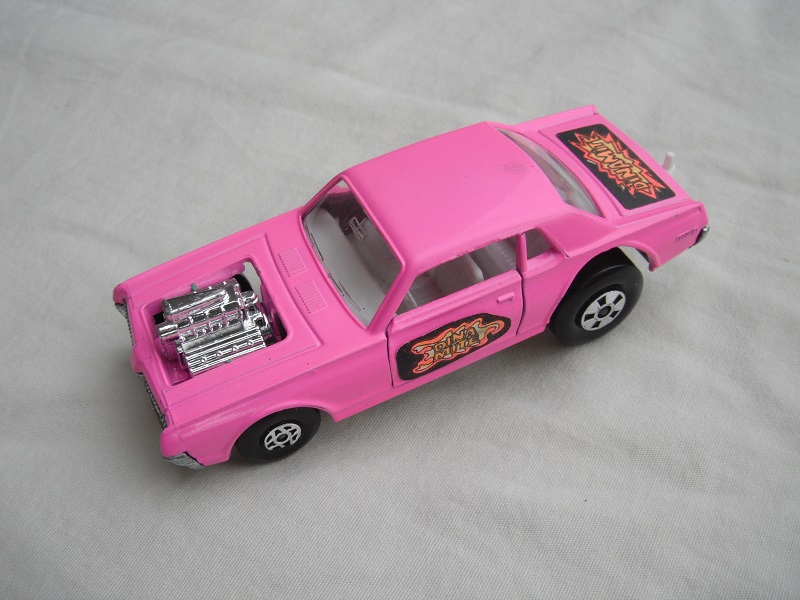 3. Med.pink body/unpainted England base/clear windows/spiro &amp; five spoke wheels/&quot;Dinamite&quot; label letters in orange.